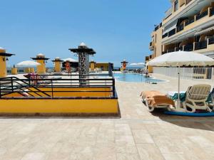 a pool with chairs and an umbrella next to a building at Puesta del sol en playa arena in Puerto de Santiago