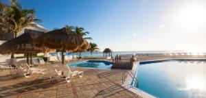 a swimming pool with chairs and umbrellas and the ocean at Comoda Suite Cancun - BEACH CONDO - 6PX in Cancún
