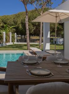 a wooden table with wine glasses and an umbrella at Villa Sancti Petri, entre el golf y la playa in Novo Sancti Petri
