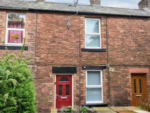 a brick house with a red door and two windows at Welsh Yard Cottage in Penrith