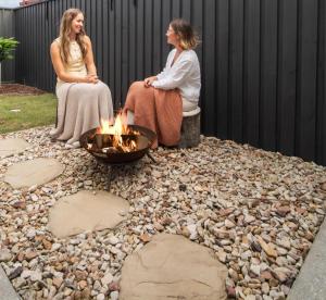 two women sitting around a fire pit on rocks at Bluebird Villa - 3min Stroll to Bokarina Beach in Bokarina +44 photos