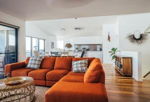 a living room with an orange couch and a kitchen at Anglesea by Bangalay in Shoalhaven Heads