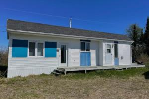 a small white house with blue windows and a porch at La petite Maison Baie-Johan-Beetz 