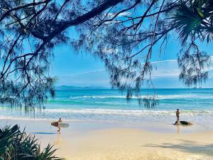 due persone che camminano sulla spiaggia con le loro tavole da surf di Byron Marvel - Luxury Byron Bay Penthouse Holiday Rental with Balcony, 4 Bedrooms, Sleeps 10 a Byron Bay