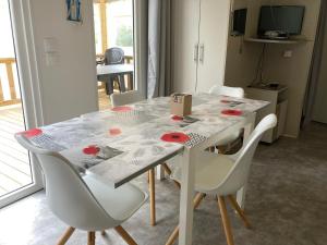 a dining room table with white chairs and a table with a box at Le Domaine des Pins in Saint-Hilaire-de-Riez