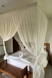 a bedroom with a white canopy bed with a wooden bench at Budha House Ubud in Ubud +11 photos