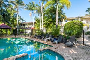 a swimming pool with chairs and palm trees at Byron Beachside 2 in Byron Bay