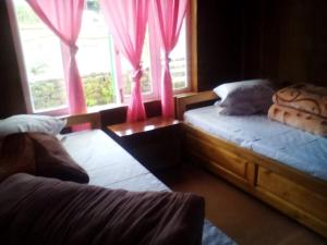 a bedroom with two beds and a window with pink curtains at Dilpali Homestay in Mirik