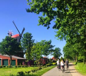 a group of people riding bikes down a road with a windmill at Ferienwohnung "Wallheckenblick Schatteburg", 95159 in Rhauderfehn