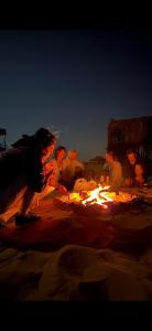 a group of people sitting around a fire in the sand at Alghyamcamp in Muntarib