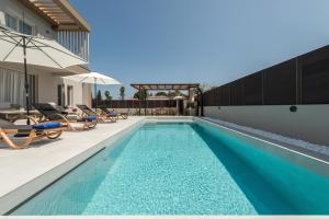 une piscine avec chaises longues et parasols à côté d'une maison dans l'établissement Villa Luna d'oro by "Elite", à Gaïtánion