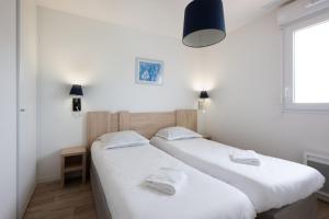two beds in a room with white walls and a window at Résidence Prestige Odalys Le Domaine des Pins in Noirmoutier-en-l'lle