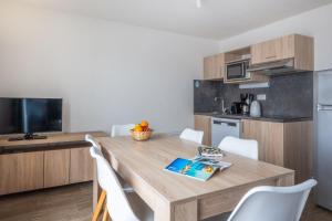 a kitchen with a wooden table and white chairs at Résidence Prestige Odalys Le Domaine des Pins in Noirmoutier-en-l'lle
