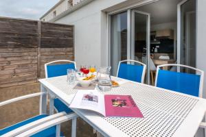 a white table with blue chairs and a book on it at Résidence Prestige Odalys Le Domaine des Pins in Noirmoutier-en-l'lle