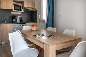 a kitchen with a wooden table and white chairs at Résidence Prestige Odalys Le Domaine des Pins in Noirmoutier-en-l'lle