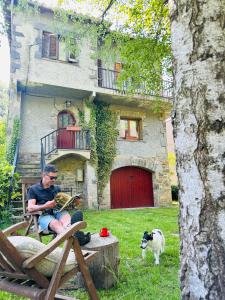 a man sitting in a chair reading a book in front of a house at La Torre de la Vall de Camprodon in Llanars