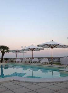 een zwembad met parasols, tafels en stoelen bij Hotel Villa Aniana in Massignano