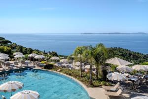 a pool with umbrellas and chairs and the ocean at Hôtel La Villa Douce in Rayol-Canadel-sur-Mer