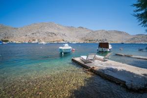 a dock with two chairs and a boat in the water at Mythos House - Seaside Retreat in Pedi in Symi
