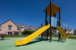a playground with a yellow slide on a green field at Résidence Odalys Horizon Morgat in Crozon
