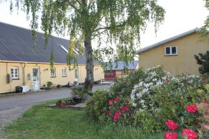 a house with a tree and flowers in a yard at Strandsegård Ferielejlighed in Ølsted