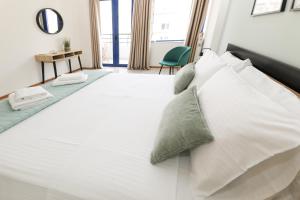 una cama blanca con almohadas blancas y una silla verde en Xenia's cozy spot, en Volos