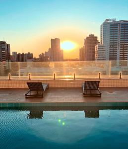 two benches sitting next to a pool of water with a city at Apartamento Sofisticado Perto de Tudo JR1304 in Maringá