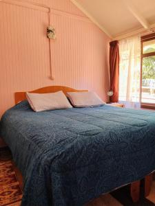 a bedroom with a bed with a blue comforter and a window at Cabaña Altos de Parra Tome 2025 - piscina temporada verano in Tomé