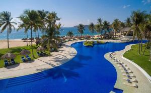 a resort swimming pool with palm trees and the ocean at Nicer Huatulco Condo in Tangolunda