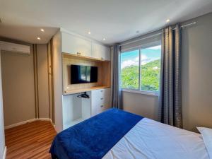 a bedroom with a bed and a tv and a window at Apartmento luxo Itapema SC in Itapema