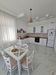 a white kitchen with a table and white chairs at Gulu Cottage House in Mərdəkan