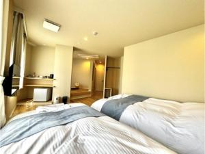 Beppu Onsen Resort Stay SPA TSURUMI - Vacation STAY 48219v في بيبو: غرفة نوم بسريرين وغرفة بها تلفزيون
