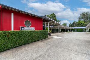 a red building with a hedge in front of it at Red Bridge Motor Inn in Woombye