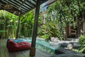 a pool with a red cushion next to a garden at MIMOYA Guest House, Sanur in Sanur +7 photos