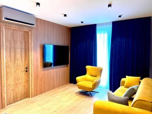 Sala de estar con 2 sillas amarillas y TV en GQ Luxe Apartments In Alliance Palace, en Batumi