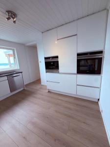 an empty kitchen with white cabinets and a wooden floor at Cherfull 2 bedrooms in Oksval