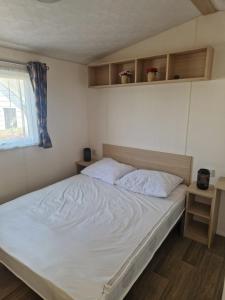a bedroom with a bed with white sheets and a window at Camping Alkenhaer Appelscha Chalet 111 in Appelscha