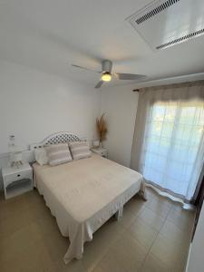 a white bedroom with a bed and a ceiling fan at Apartamento en la playa con piscina in Ciutadella