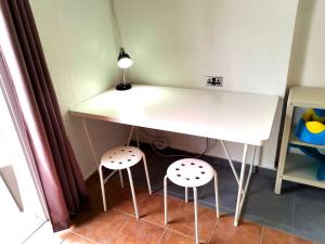 a white table with two stools under it with a lamp at Spacious Larnaca Beach Apartment in Larnaka
