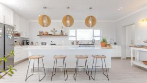a kitchen with a white counter and bar stools at Pondok Straat - Agulhas in Agulhas