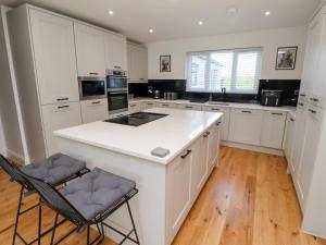 une cuisine avec des armoires blanches et un îlot blanc avec deux chaises dans l'établissement Rose Cottage, à Alnwick