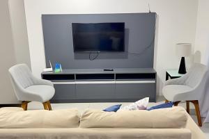 sala de estar con TV y 2 sillas blancas en Edf Time 1503 | Piscina | Academia | Jacuzzi, en Maceió
