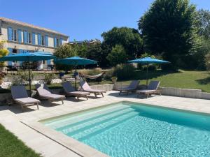 a swimming pool with chairs and umbrellas next to a building at Le Clos de Chenac in Chenac-sur-Gironde