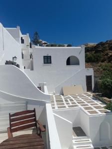 a white house with a wooden chair and stairs at IOS ALL INN ROOMS - Sea View in Ios Chora