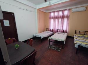 a room with three beds and a table and a window at Nirmali Homestay in Guwahati