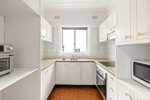 a white kitchen with white cabinets and a window at Comfortable & Affordable Stay in Padstow - Queen Room Retreat - Shared Bathroom in Padstow +30 photos