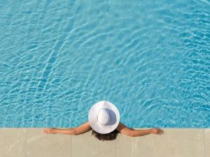 a woman in a hat laying on the edge of a swimming pool at Jumeirah Messilah Beach Kuwait in Kuwait