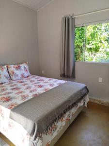 ein Bett in einem Schlafzimmer mit Fenster und Tagesdecke in der Unterkunft Chalé do Ypê 2 in Pirenópolis