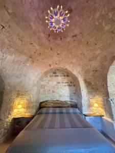 a bed in a stone room with a chandelier at Masseria Mazzalorsa in Alberobello