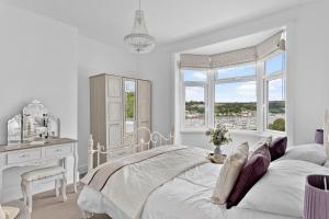 a white bedroom with a bed and a desk and window at River Retreat in Kingswear